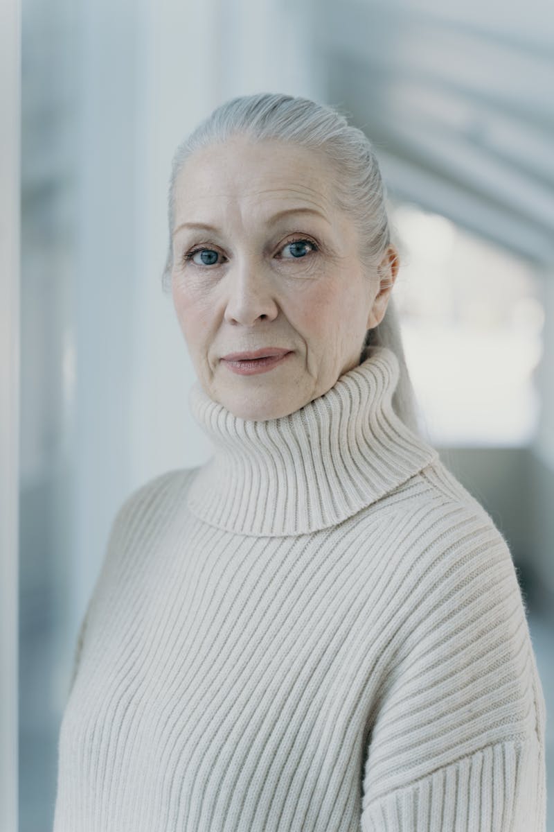 Close-up portrait of a senior woman with grey hair in a cozy turtleneck sweater indoors.